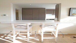 Une cuisine moderne avec des meubles blancs et un plan de travail blanc. On y trouve deux chaises blanches avec des pieds en métal.