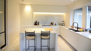 Una cocina moderna con una isla central, dos taburetes de bar, un lavaplatos integrado y una ventana con persianas.