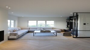 Una sala moderna con un sofá modular, una mesa de centro de vidrio y un piso con patrón de espiga.