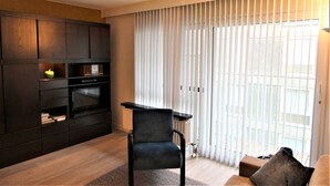 A modern living room with a dark wood cabinet, a black chair, and a large window with vertical blinds.