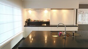 Una cocina moderna con encimera negra, armarios blancos, un lavamanos de acero inoxidable y una ventana que proporciona luz natural.