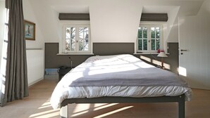 Un dormitorio con una cama, dos ventanas, un radiador, una puerta y un cuadro en la pared.