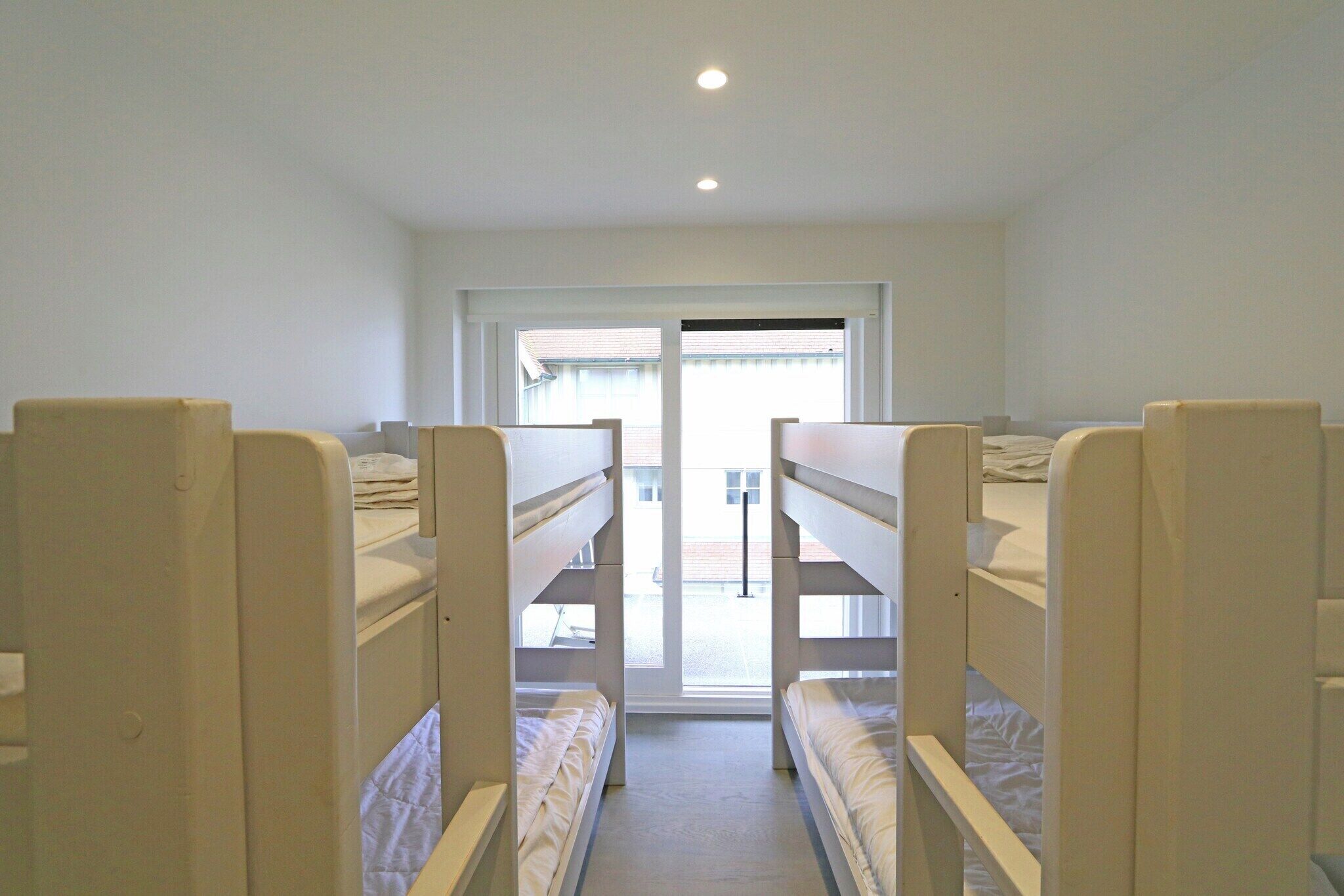 A room with bunk beds arranged in a row, a window with a view of the outside, and a door leading to an outdoor area.