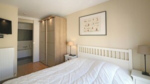Een slaapkamer met een bed, een nachtkastje, een wandtelevisie, een ingelijste foto en een schuifdeurkast.