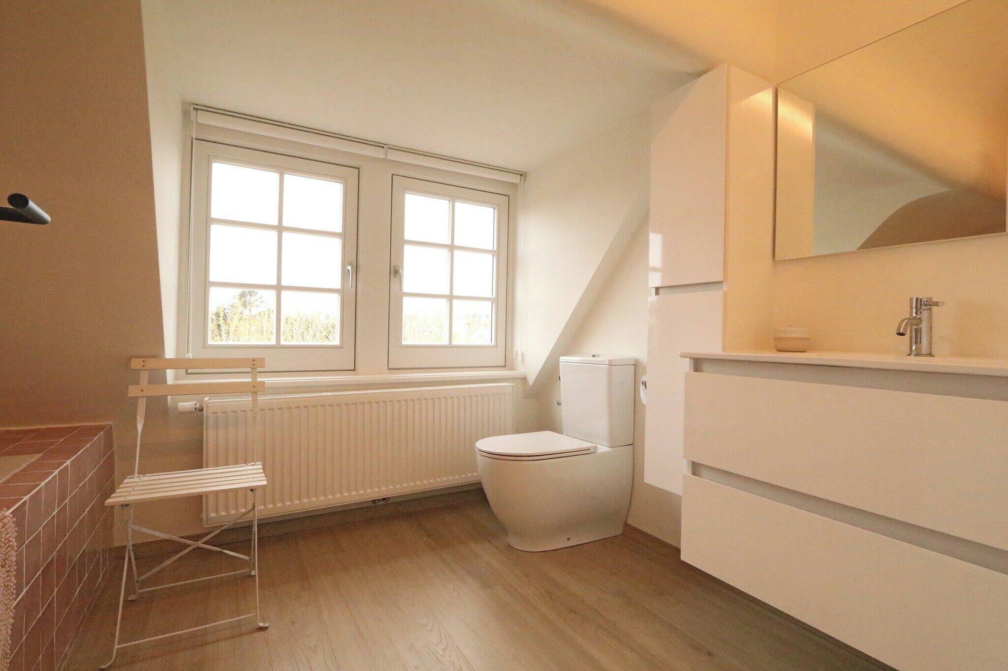 Et badeværelse med toilet, radiator, vindue og spejl.