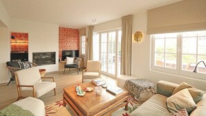 Un salon spacieux doté d’une cheminée, de sièges confortables, d’une table basse et de grandes fenêtres offrant une vue sur l’extérieur.