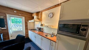 A compact kitchen with a sink, stove, microwave, and a clock on the wall. - Holiday Home in Elim near Slagharen Park (Elim)