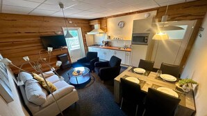 A compact living space with a sofa, a dining table set for four, a kitchen area with a stove and microwave, and a television on the wall. - Holiday Home in Elim near Slagharen Park (Elim)