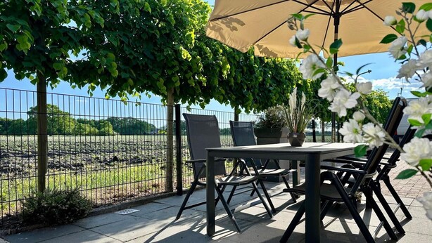 An outdoor patio with a table and chairs under a canopy, surrounded by a fence and greenery. - Holiday Home in Elim near Slagharen Park (Elim)