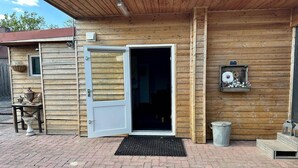 A wooden building with a door open to a dark interior, a small table with pots, and a metal trash can outside. - Holiday Home in Elim near Slagharen Park (Elim)