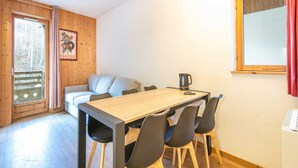 Ein Zimmer mit Holzwänden, einem Esstisch, Stühlen, einer Couch und einer Kaffeemaschine.