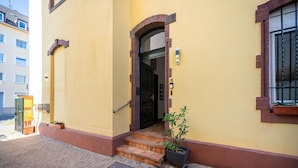 Un bâtiment jaune avec une porte noire et un petit escalier menant à l’entrée.