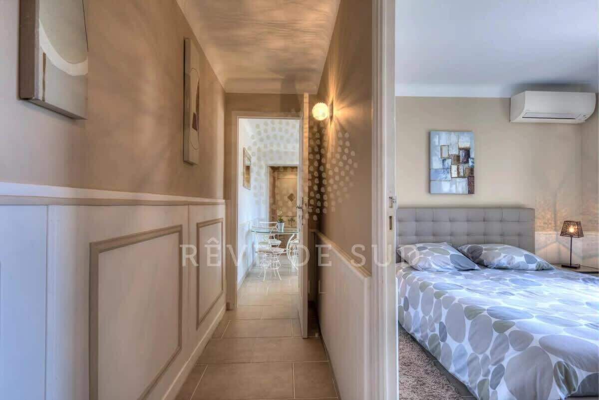 Een hotelkamer met een bed, nachtkastje en een bijzettafeltje. Er is een gang die naar een andere kamer leidt.