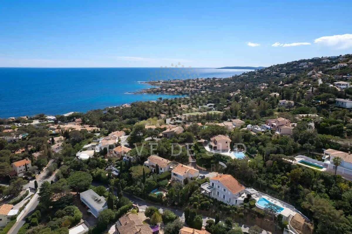 Vue aérienne d’une zone résidentielle côtière, avec des maisons, une mer d’un bleu limpide et une petite plage.