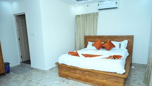 Una cama bien hecha con ropa de cama blanca y almohadas naranjas, un cabecero de madera y un aire acondicionado en el techo.