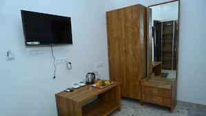 Una habitación pequeña y sencilla con un armario de madera, un escritorio de madera con espejo, un televisor fijado a la pared y piso de baldosas.