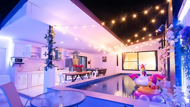 Un espace piscine intérieur moderne, comprenant une table et des chaises pour les repas, une table de billard et des jeux gonflables.