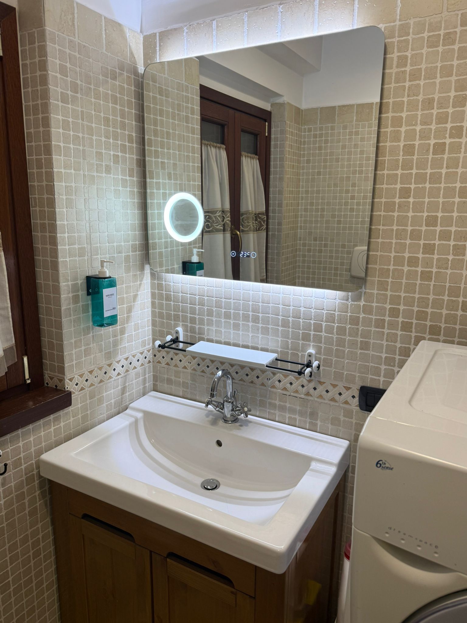 Une salle de bain avec un lavabo blanc, un miroir doté d’une lampe ronde et un porte-serviettes.
