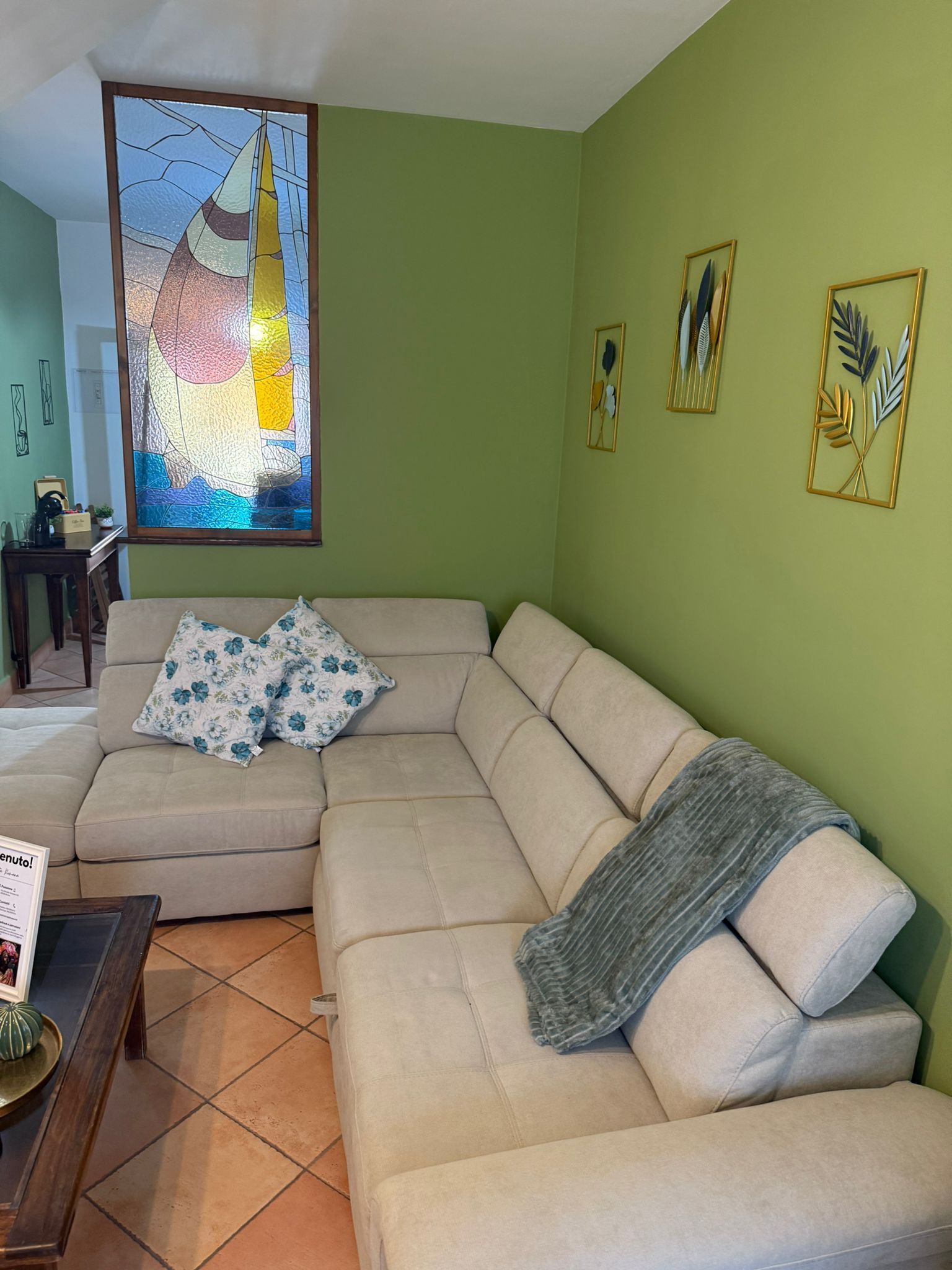 Un salon avec un canapé d’angle beige, une table basse et un tableau représentant un voilier.