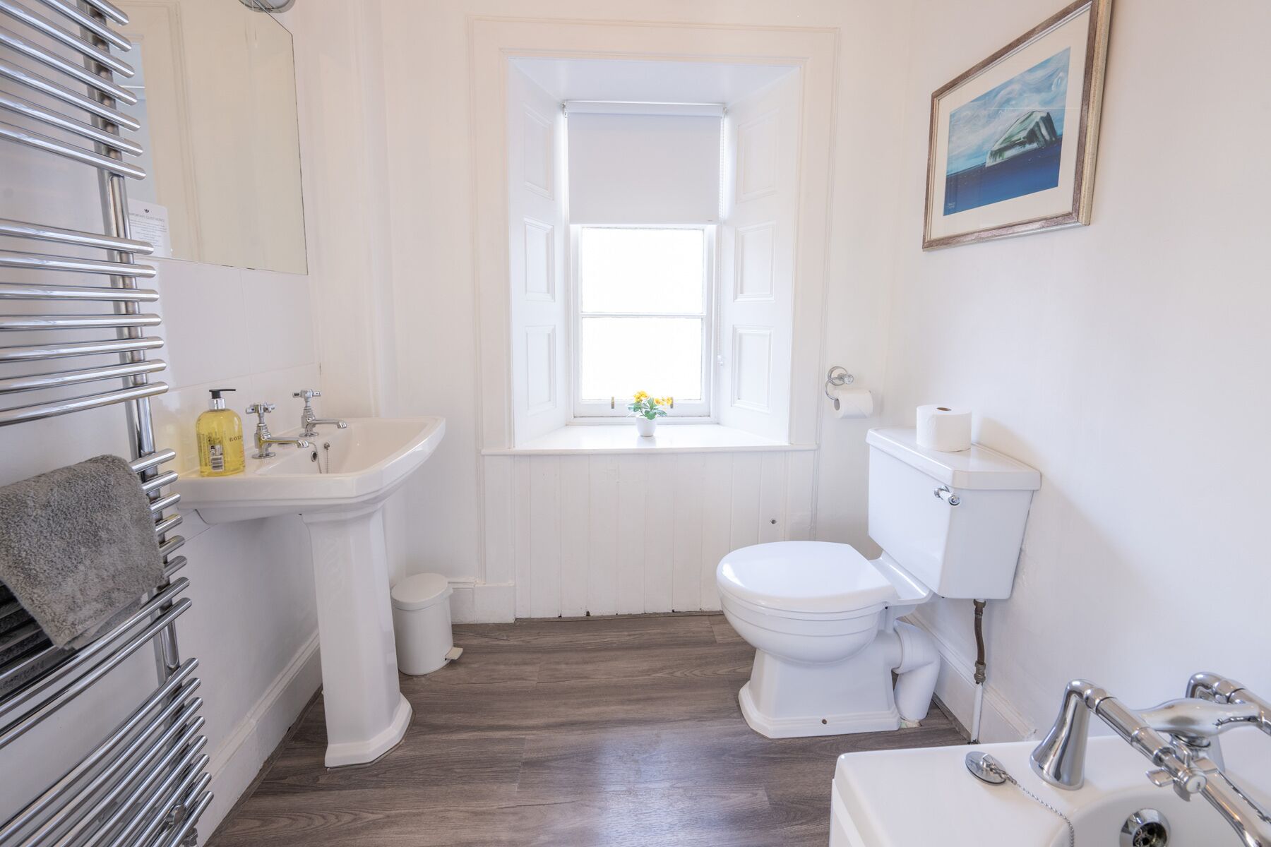 A bathroom with a white sink, toilet, and bathtub. There is a window with a view of the sky and a small plant on the windowsill.