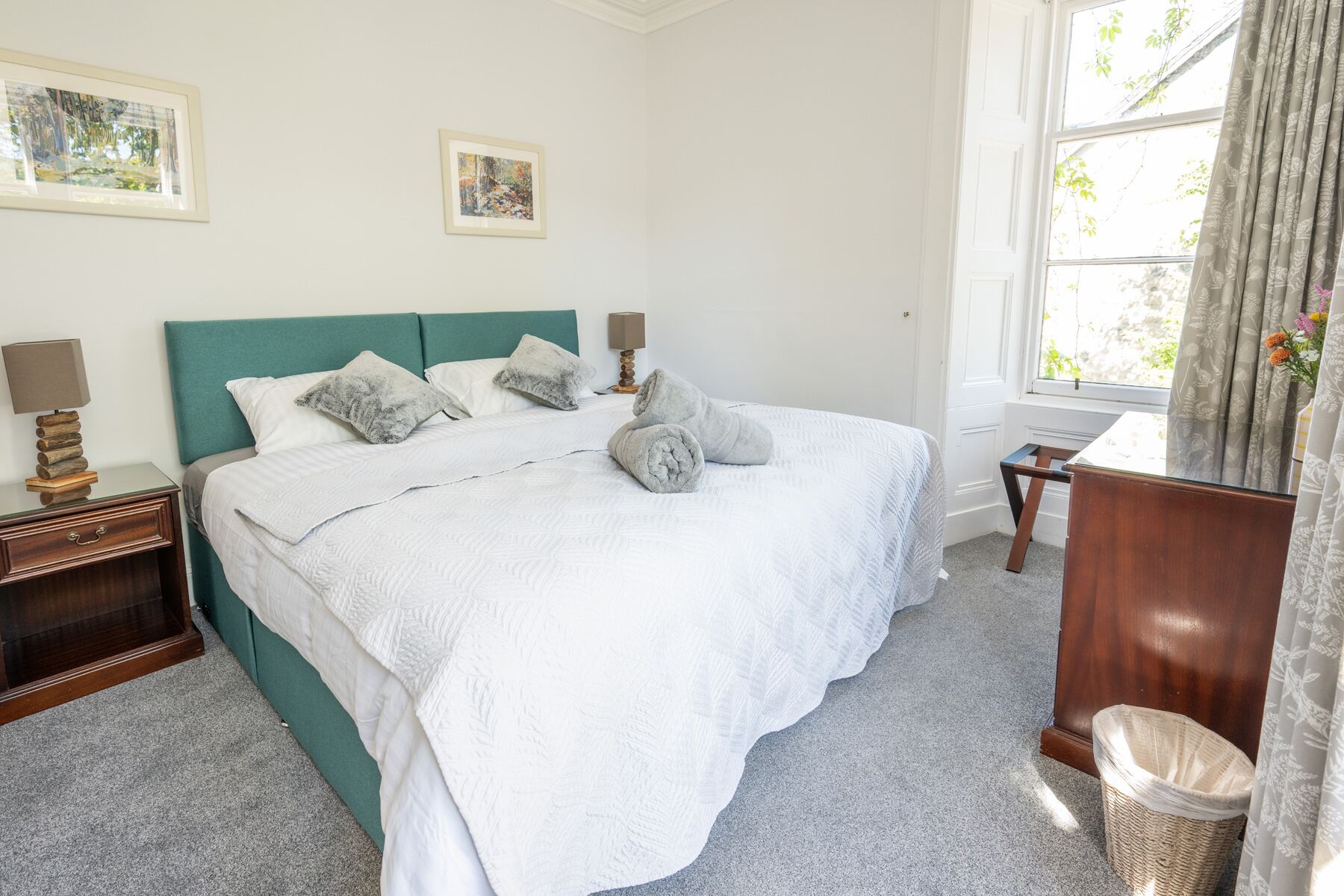 A neatly made bed with white bedding, a teal headboard, and two bedside lamps.