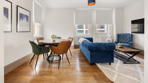 Ein modernes Wohnzimmer mit Essbereich, einem blauen Sofa und einem an der Wand befestigten Fernseher.