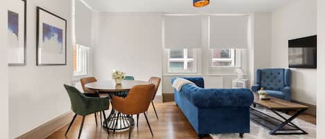 Una sala de estar moderna con comedor, un sofá azul y un televisor montado en la pared.