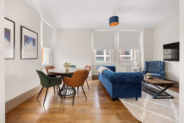 A modern living room with a dining area, a blue sofa, and a television mounted on the wall.