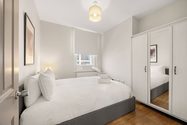A modern bedroom with a large bed, a wardrobe, and a staircase leading to an upper level.