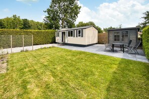 Un petit bâtiment d’un seul étage, doté d’une porte et de fenêtres, d’une terrasse avec une table et des chaises, et d’une pelouse bien entretenue.