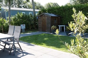 A small wooden shed in a garden with a lawn, a metal table, and a chair.