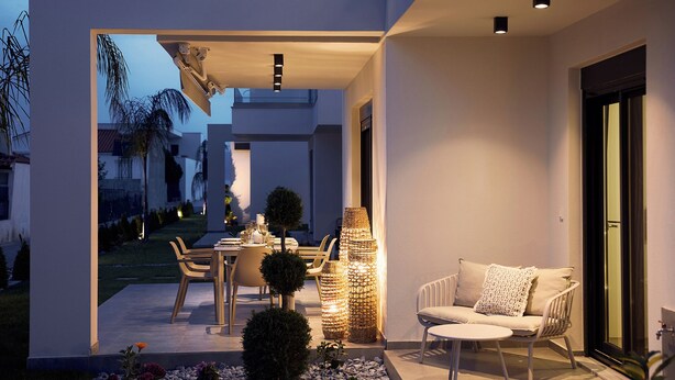 Ein Terrassenbereich im Freien mit Esstisch, Stühlen und einer Couch. Dekorative Lichter und ein kleiner Baum sind vorhanden.