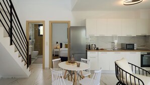 Eine moderne Küche mit weißen Schränken, einem Edelstahl-Kühlschrank und einer Mikrowelle. Es gibt einen Essbereich mit einem runden Tisch und weißen Stühlen.