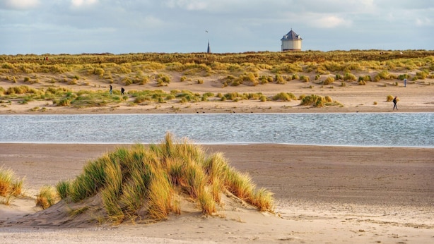 Une plage avec des dunes de sable et une étendue d’eau.