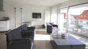 Une chambre d’hôtel moderne équipée d’un canapé, d’une petite table, d’une télévision et d’un balcon offrant une vue sur les bâtiments.