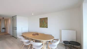 A modern meeting room with a round table, six chairs, a whiteboard, and a colorful abstract painting.