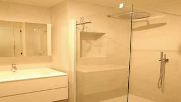 Een moderne badkamer met een douchecabine van glas, een witte wastafel en een grote spiegel.
