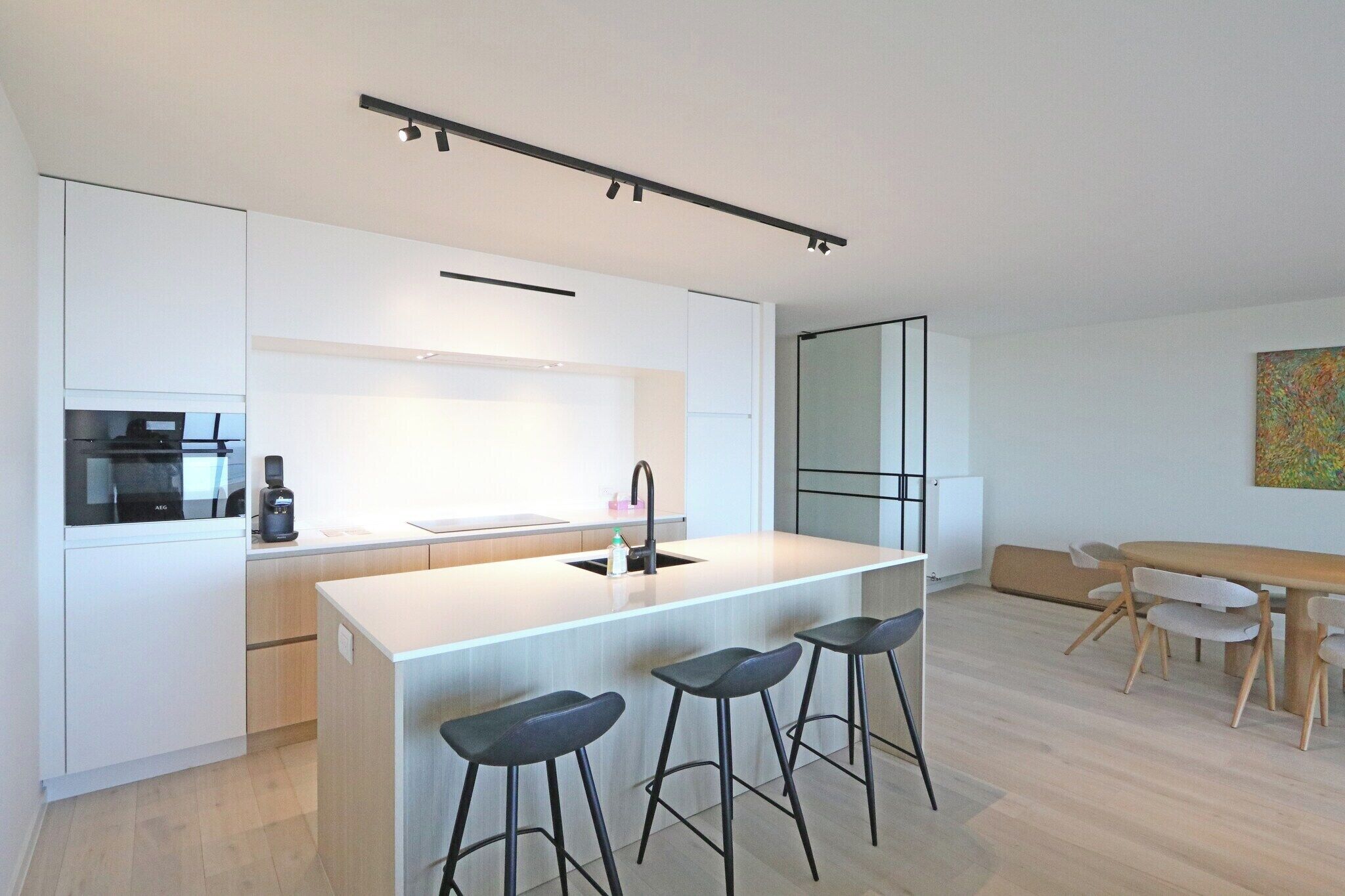 Een moderne keuken met een centraal eiland, barkrukken, een eettafel met stoelen en een koffieapparaat.