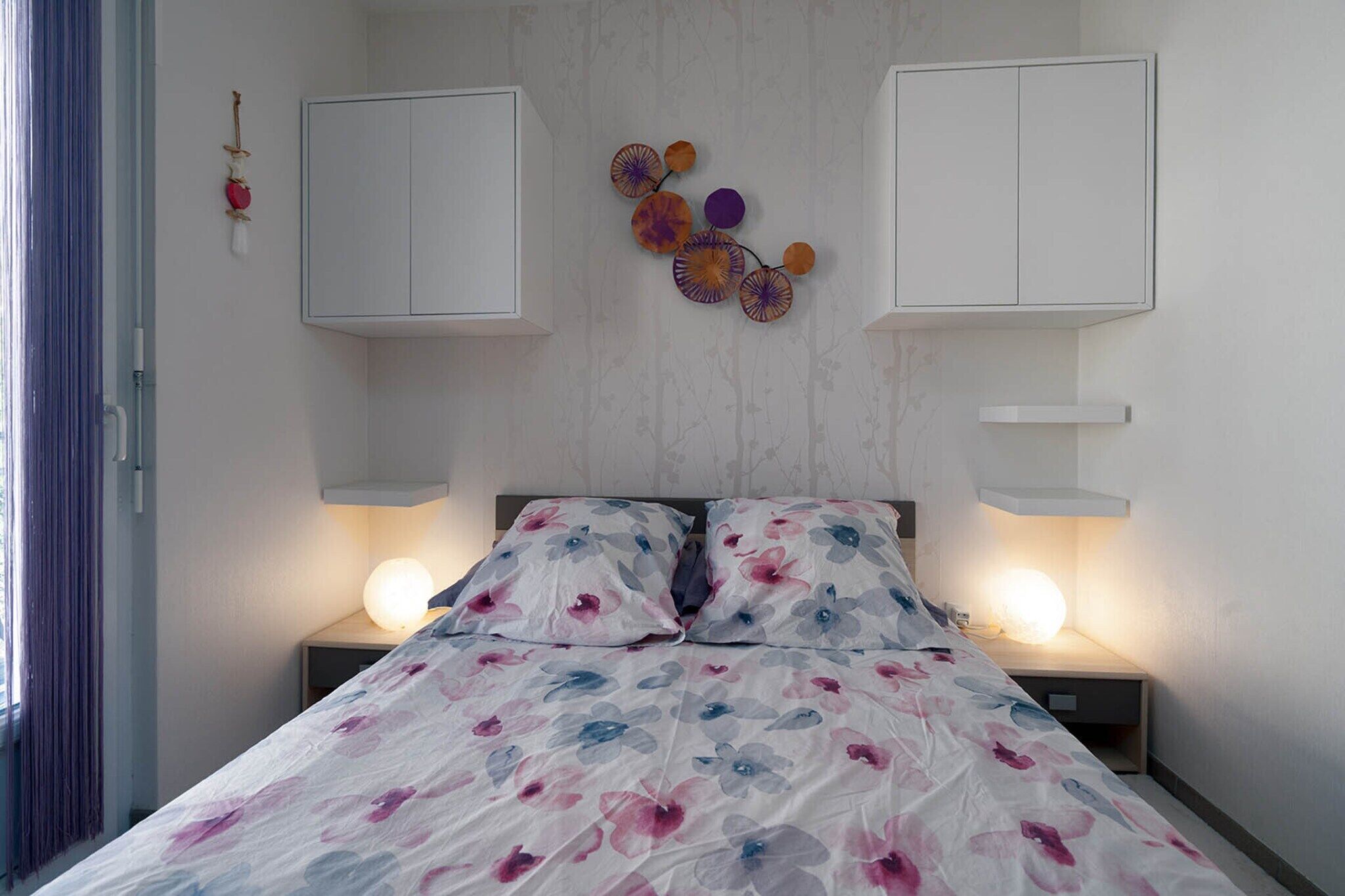 Een slaapkamer met een bed, twee nachtkastjes met lampen, een wandplank en een decoratieve wandversiering.