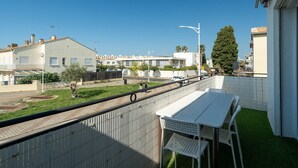 A balcony with a white table and chairs, overlooking a street with buildings and a clear sky. - Apartment in Grau du Roi near the Beach (Le Grau-du-Roi)