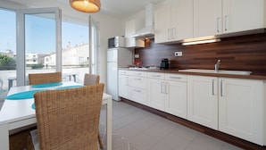 A modern kitchen with white cabinets, a wooden countertop, and a dining area with wicker chairs and a table. - Apartment in Grau du Roi near the Beach (Le Grau-du-Roi)