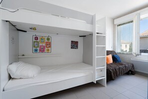 A bunk bed room with a white bed, a lower bunk, and a shelf with children's artwork. - Apartment in Grau du Roi near the Beach (Le Grau-du-Roi)
