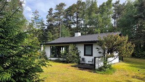A small, single-story house with a porch, surrounded by trees and grass.