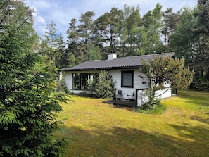 A small, single-story house with a porch, surrounded by trees and grass.