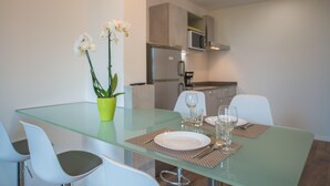 Un espace repas moderne avec une table en verre, des chaises blanches et une orchidée en pot.