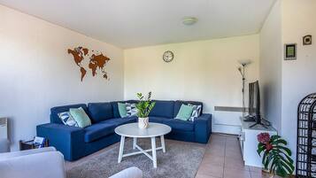 Un salon avec un canapé bleu, une table basse blanche, une carte du monde accrochée au mur, une horloge et une plante.