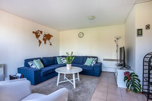 A living room with a blue sofa, a white coffee table, a world map on the wall, a clock, and a plant.