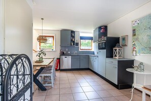 Cocina compacta con armarios grises, lavavajillas, microondas y un pequeño comedor con mesa y sillas.