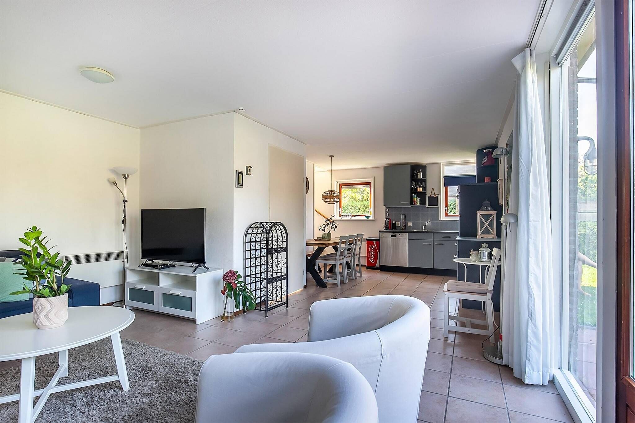 Un salon moderne avec un téléviseur à écran plat, des canapés blancs, une table à manger et une cuisine en arrière-plan.