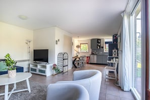 A modern living room with a flat-screen TV, white sofas, a dining table, and a kitchen in the background. - Holiday Home in Grou with Whirlpool & Terrace (Grou)